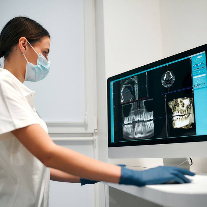 Female dentist with mask looking at dental scans on computer