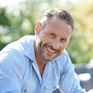 Man with facial hair sitting outside and smiling
