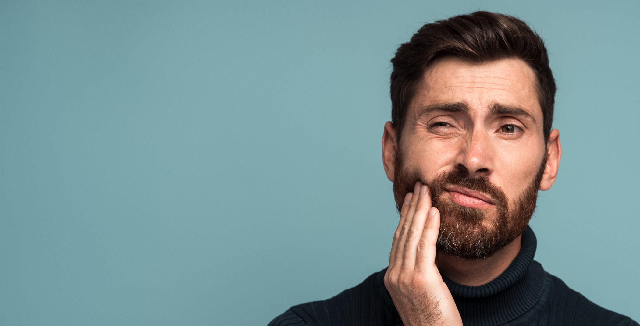 Bearded man rubbing his jaw in pain