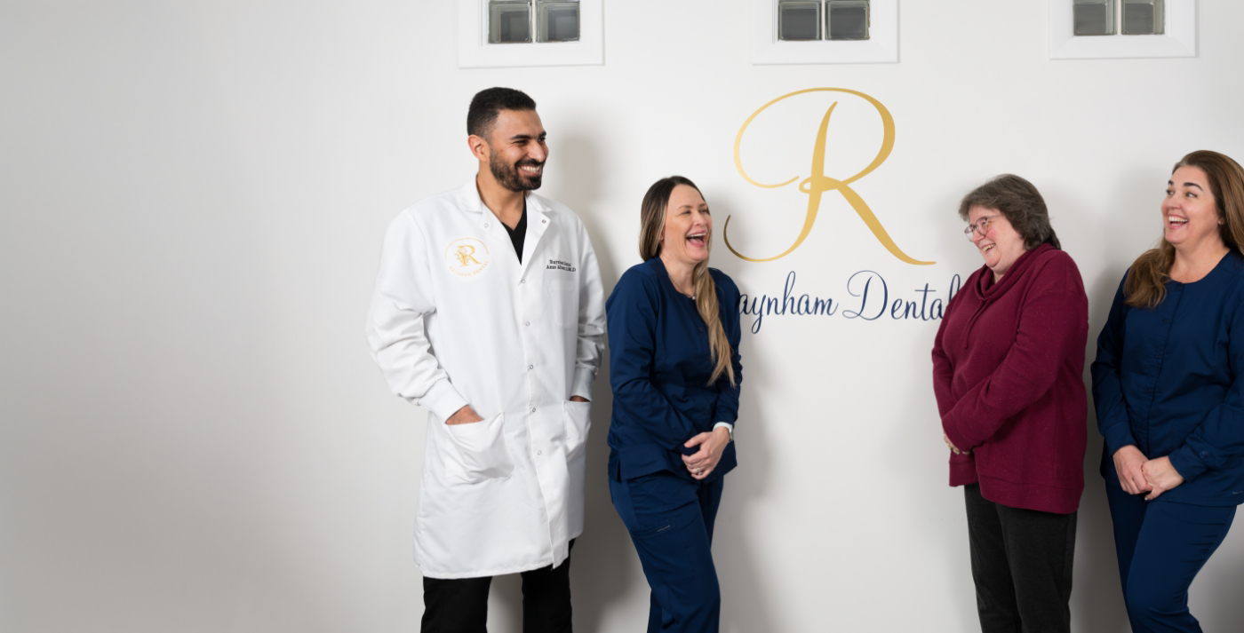 Dentist in Raynham and team laughing in front of wall