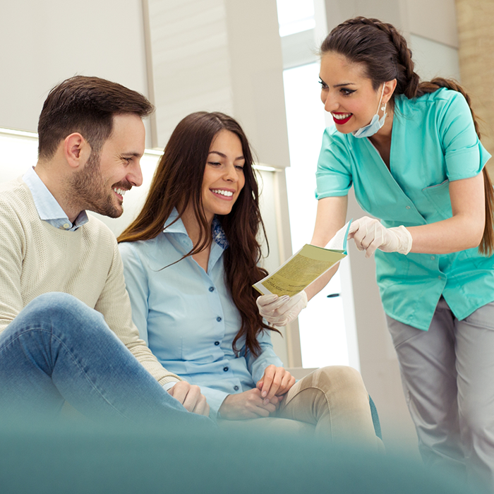 Female dental team member showing form on clipboard to two patients