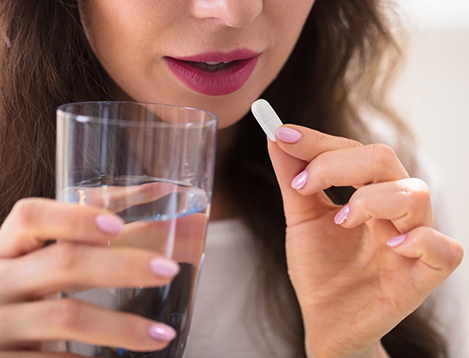 Woman holding glass of water and about to take pill