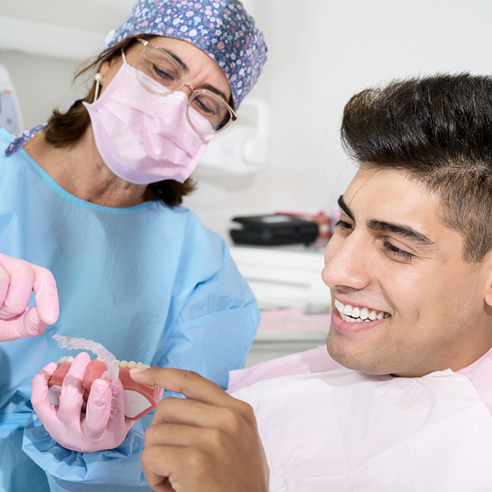 Female dentist with mask showing Invisalign aligner to male patient