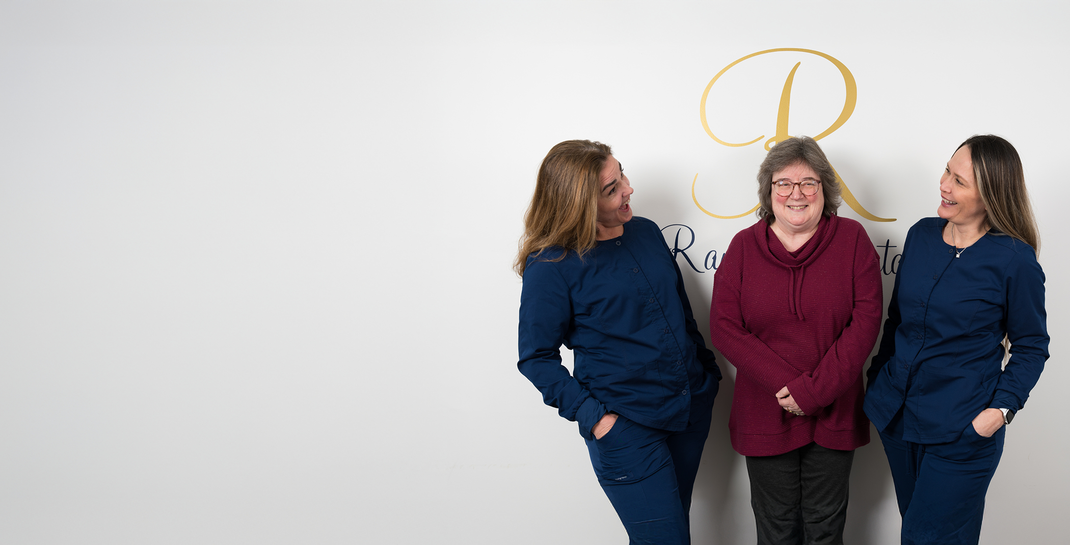 Three women in Raynham standing in front of wall and smiling