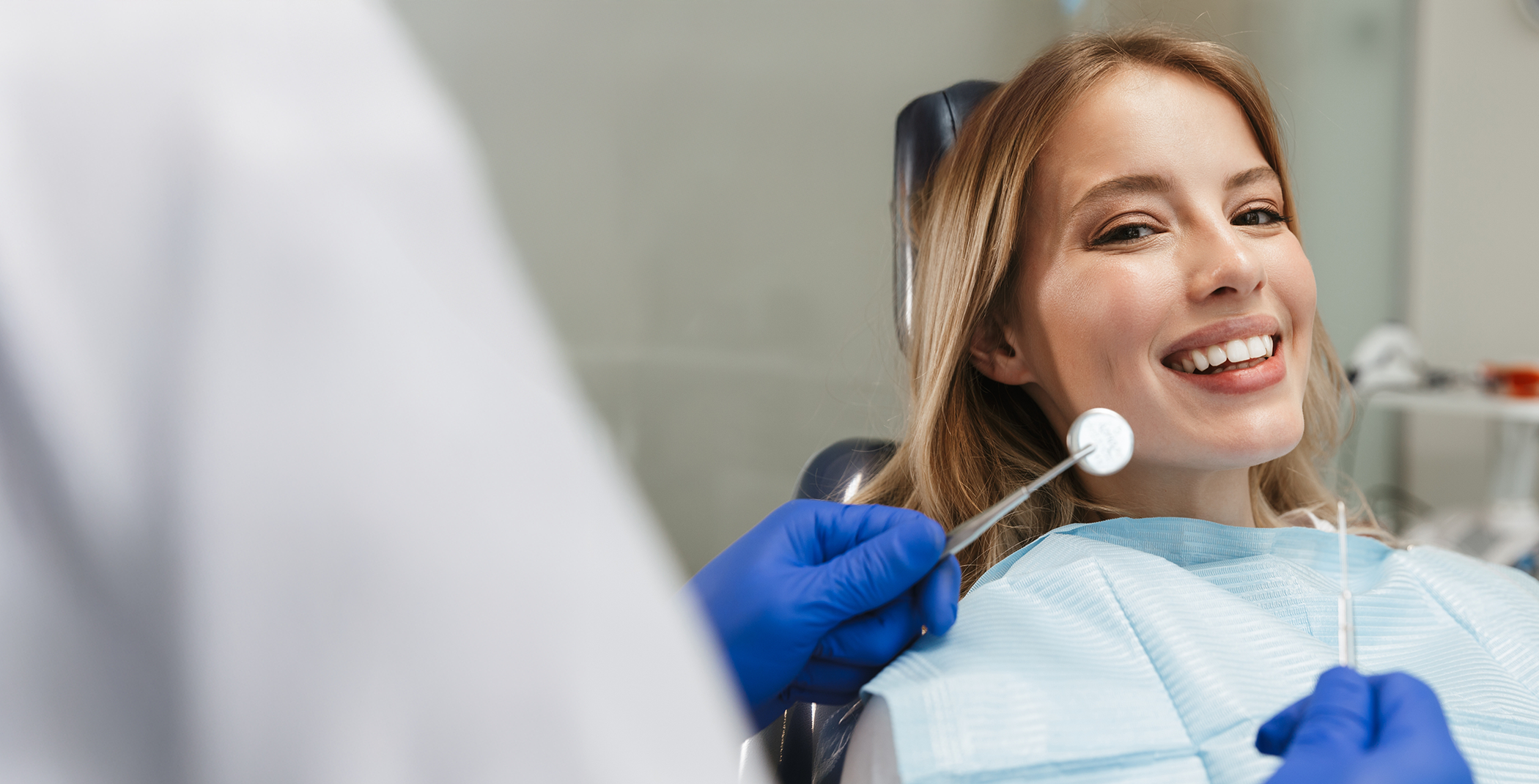 Woman in dental chair smiling at dentist holding dental instruments