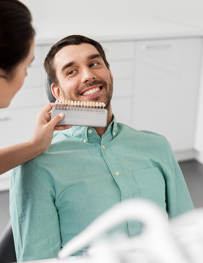 Dentist comparing patient’s teeth with shade tabs after whitening